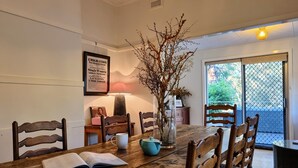 A dining area with a wooden table, chairs, a vase with branches, a framed picture, and a lamp. - The Mia Mia Newstead - Pet Friendly Country Retreat close to town (Newstead)