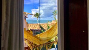 A room with a large window overlooking a beach, a hammock, and a door.