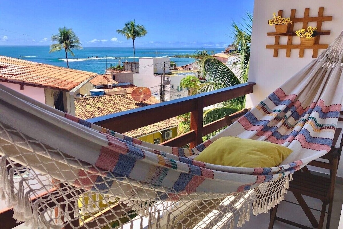 A hammock on a balcony with a view of the ocean and palm trees.