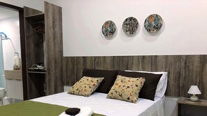 A neatly made bed with a green bedspread, two rolled towels, and three decorative wall pieces.