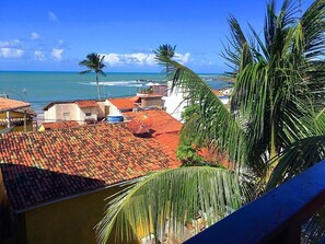 Vista costera con techos de tejas rojas, palmeras y un cielo azul despejado.