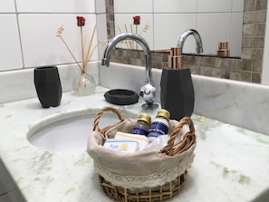 Un lavamanos con una cesta tejida que contiene artículos de tocador, un florero negro y difusores de aroma.