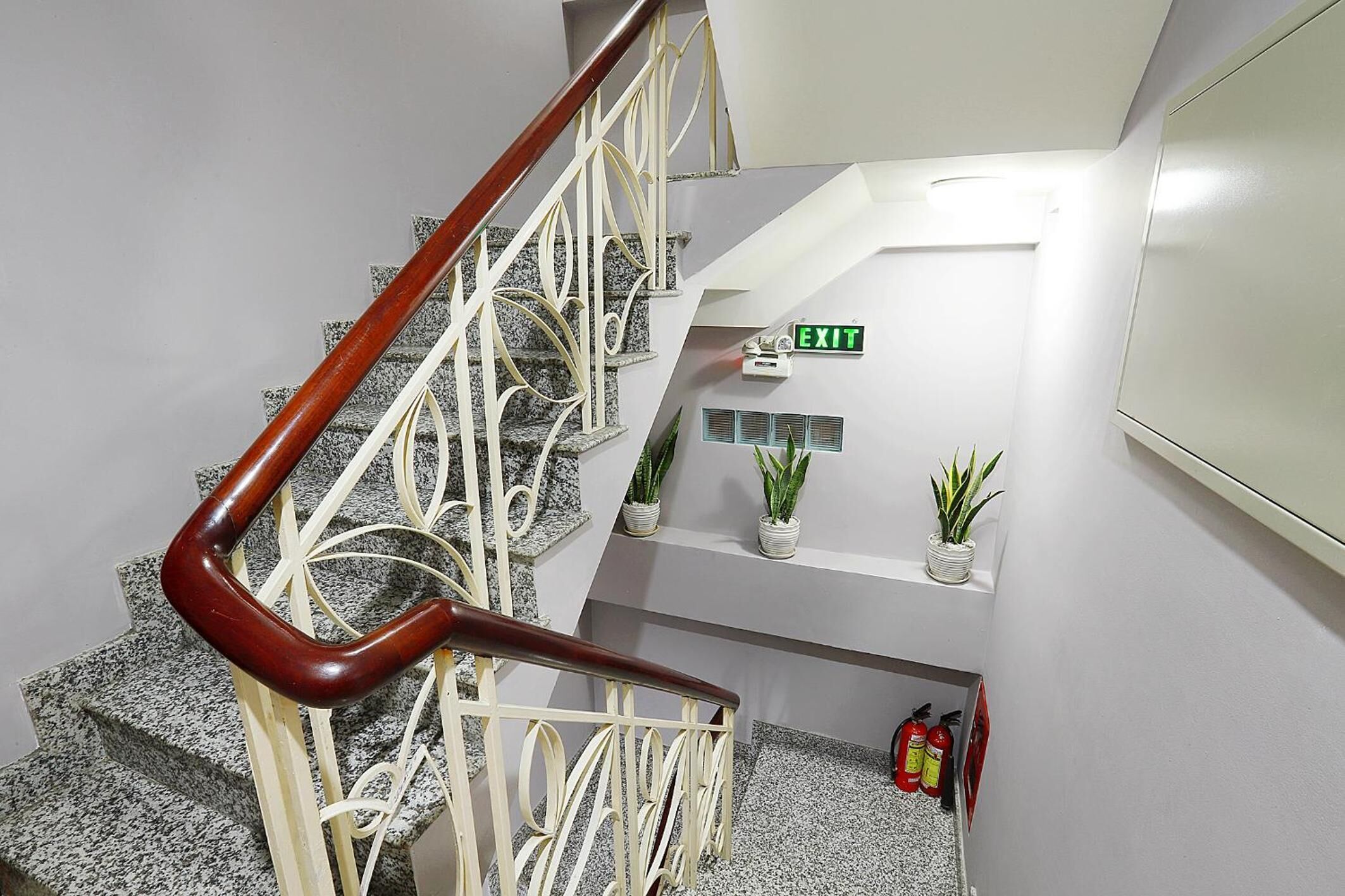 A staircase with a wooden handrail, granite steps, and a white wall with an exit sign.