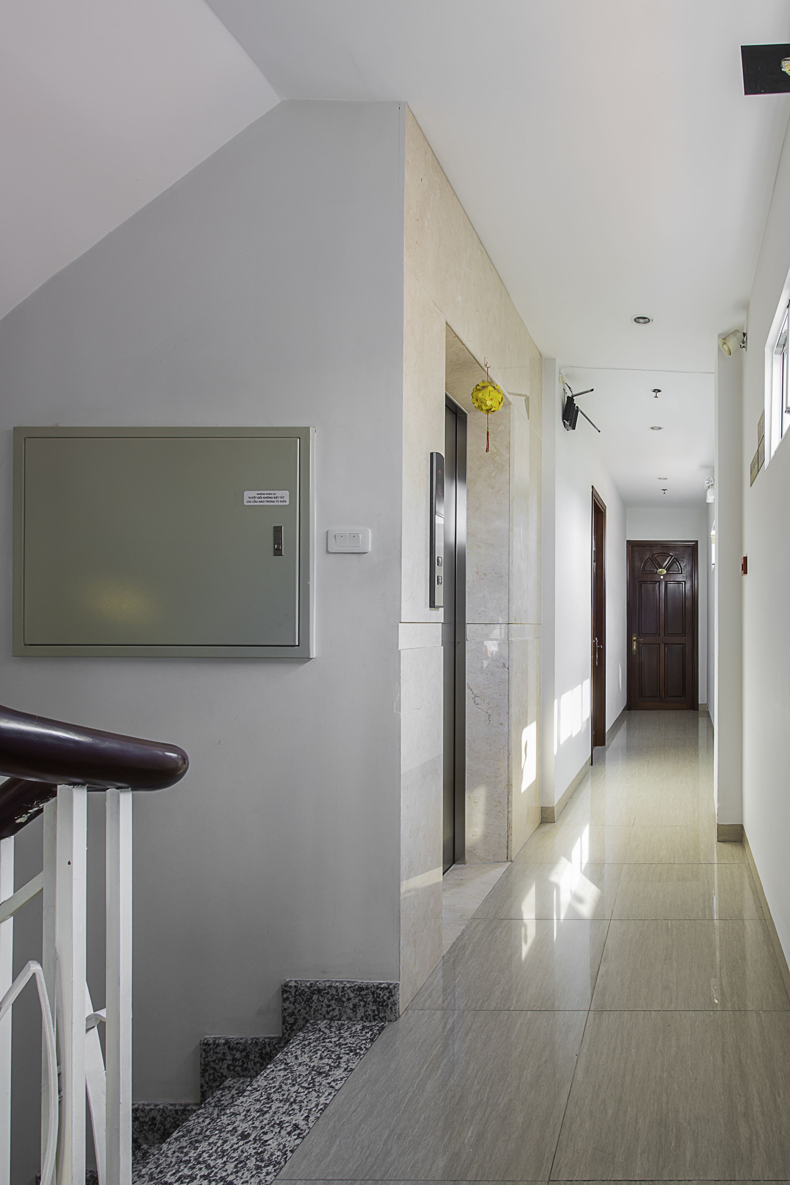 En modern hall med ett marmorgolv, en väggmonterad elcentral, en dörr längst in och en trappa med en dekorativt mönstrad matta.