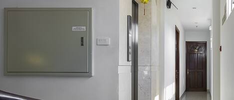 En modern hall med ett marmorgolv, en väggmonterad elcentral, en dörr längst in och en trappa med en dekorativt mönstrad matta.
