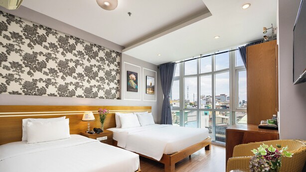A hotel room with two beds, a large window with a city view, a wooden headboard, and a wicker chair. - Lucky Star Hotel 266 De Tham (Ho Chi Minh City)