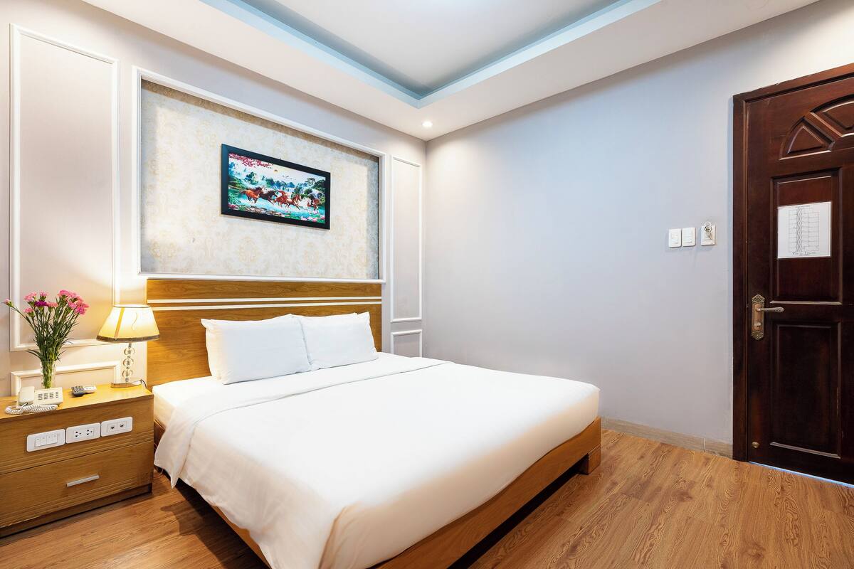 Une chambre d’hôtel avec un lit, une table de chevet, une lampe et un tableau encadré au mur.