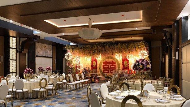 A banquet hall with round tables, white chairs, and a floral backdrop. - J7 Plaza Hotel (Iloilo)
