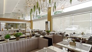A modern restaurant with high ceilings, hanging plants, and a variety of seating options including booths and tables.
