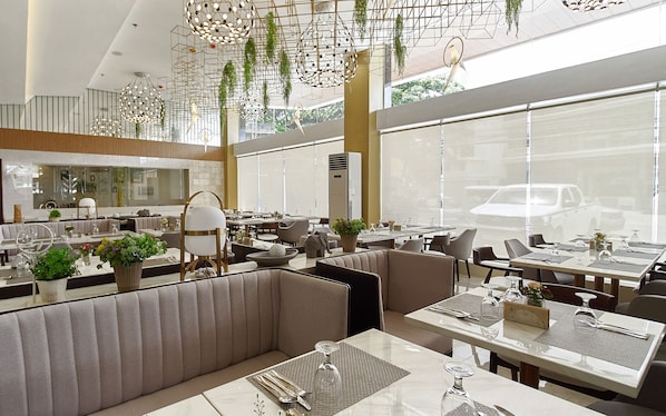 Um restaurante moderno com pé-direito alto, plantas penduradas e diversas opções de assentos, incluindo cabines e mesas.