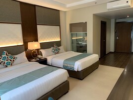A hotel room with two beds, a bathroom with a mirror and sink, and a door leading to another room.