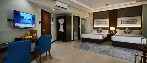 A hotel room with two beds, a desk with a TV, a robe, and a shower area.