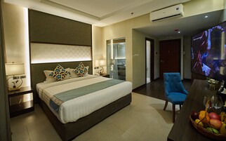 Habitación de hotel con una cama grande, televisión, escritorio con un frutero y un sillón azul.