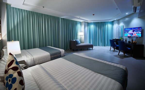A hotel room with two beds, a desk, a chair, a TV, and a lamp. - J7 Plaza Hotel (Iloilo)