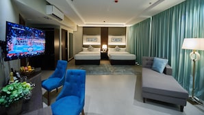 A hotel room with two beds, a TV, a sofa, and a desk with a lamp.