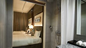 A modern bathroom with a shower, a sink with a marble countertop, and a bed with a headboard.