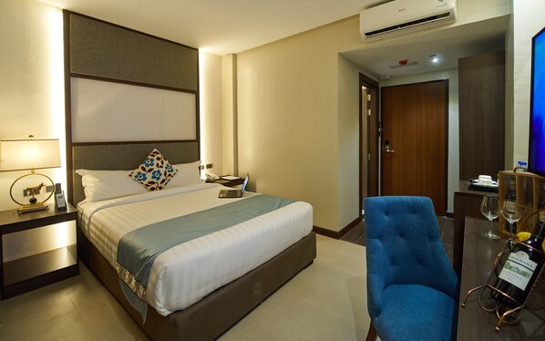 Habitación de hotel con cama, escritorio con laptop, silla, minibar y televisor.