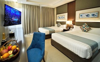 A hotel room with two beds, a TV displaying a boxing match, a fruit basket, and a blue armchair.
