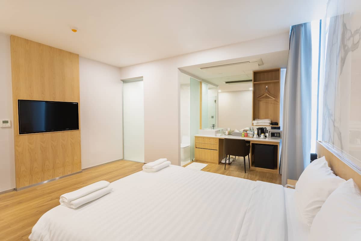 Moderni hotellihuone, jossa on suuri sänky, työpöytä, peili ja televisio.