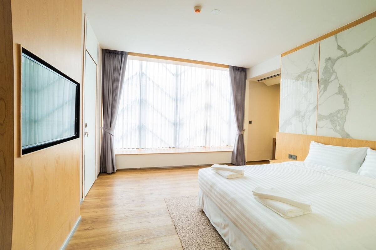 Hotellihuone, jossa on suuri sänky, seinälle asennettu televisio ja ikkuna, jossa on verhot.