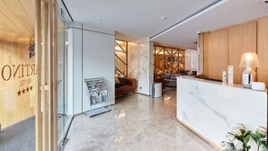 Eine moderne Hotelhalle mit einer Marmor-Rezeption, einer Sitzecke inklusive Sofa und Sesseln sowie einer Holzwand mit einem Schild.
