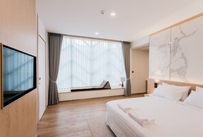 A modern hotel room with a large bed, a TV mounted on the wall, a window with curtains, and a wooden floor. - Artino Hotel (Bangkok)