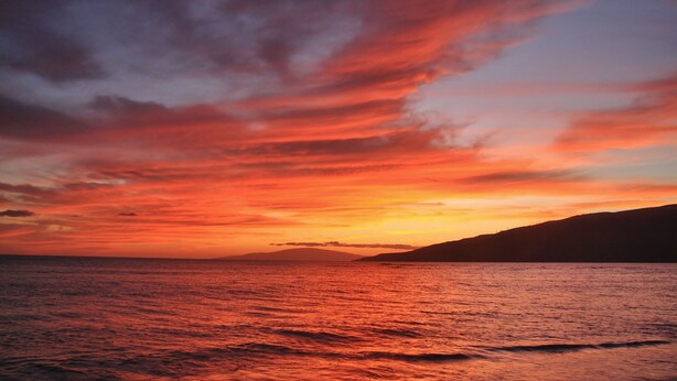 Un coucher de soleil sur une mer calme, avec une côte lointaine à l’horizon.