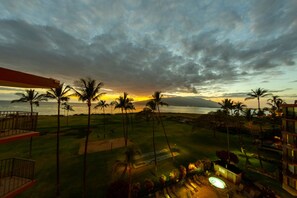 A resort with a view of the ocean at sunset, palm trees, and a pool area.