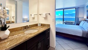Une salle de bain moderne avec un comptoir en granit, un grand miroir et une vue sur un balcon donnant sur un paysage pittoresque.