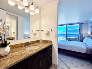 A modern bathroom with a granite countertop, a large mirror, and a view of a balcony with a scenic landscape.