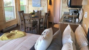 Een gezellig interieur van een chalet met een bed, een eettafel met stoelen, een keukenhoek en een raam met uitzicht.