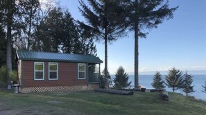 Una piccola cabina con tetto in metallo, un portico e vista sull'acqua.