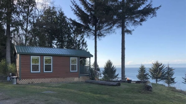 A small cabin with a metal roof, a porch, and a view of the water.