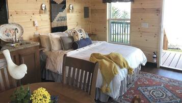 Ein gemütliches Schlafzimmer in einer Holzhütte mit Bett, Nachttisch und Fenster mit Blick ins Freie.