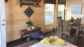 A cozy room with a bed, a small table with a plant, a chair, a window, and a wall-mounted heater.