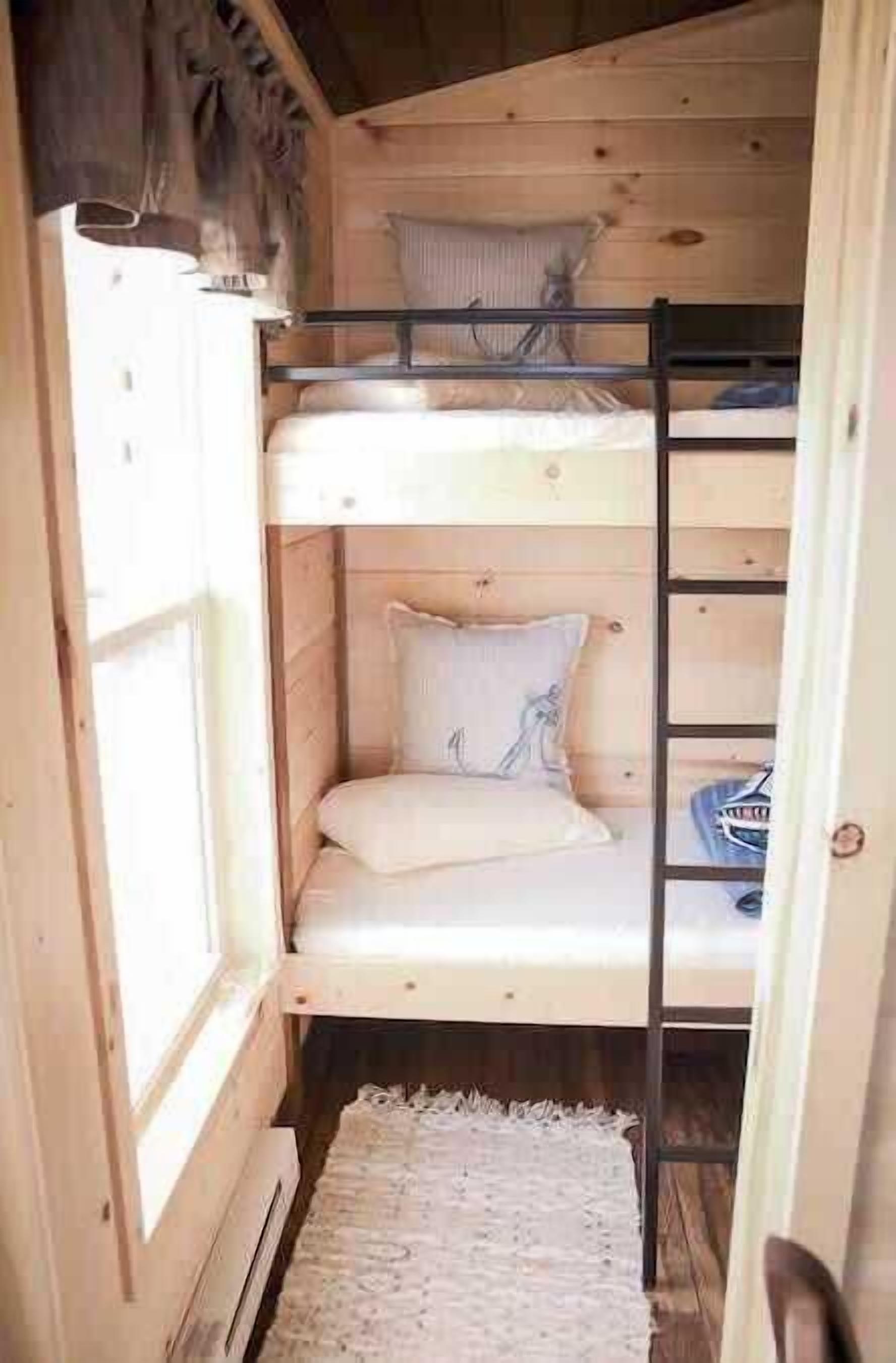 A small, wooden cabin room with bunk beds, a window, and a white rug.