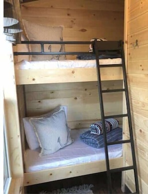 En våningssäng med en stege, träväggar och ett fönster.