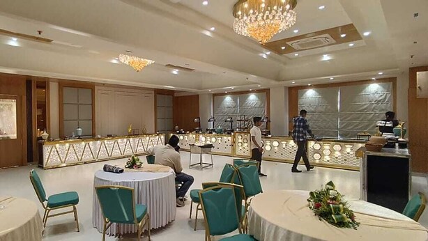 Une salle de banquet avec des tables rondes, des chaises vertes et une scène.