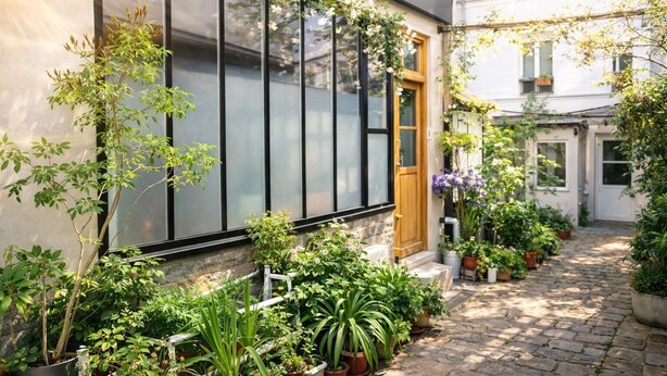 A courtyard with potted plants, a wooden door, and a window with a black frame. - Atelier d'artiste / artist loft / 35m2 (Paris)
