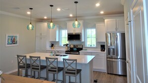 A modern kitchen with white cabinets, a central island with bar stools, stainless steel appliances, and pendant lighting. - Closest to the Beach @ Lost Key + Game Room (Pensacola)