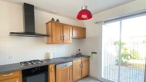 A modern kitchen with wooden cabinets, a gas stove, and a red pendant light. - Charming Renovated House with Garden, 300m from Beach, WiFi Included (Bretignolles-sur-Mer)