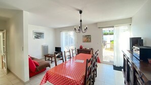 A dining area with a red table, chairs, and a chandelier. There is a television and a cabinet in the background. - Charming Renovated House with Garden, 300m from Beach, WiFi Included (Bretignolles-sur-Mer)