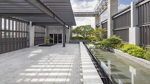 Un edificio moderno con una galleria coperta, un elemento d'acqua riflettente e vegetazione.