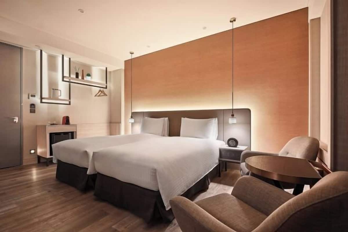 A modern hotel room with a large bed, a desk, a chair, and a wall-mounted shelf.