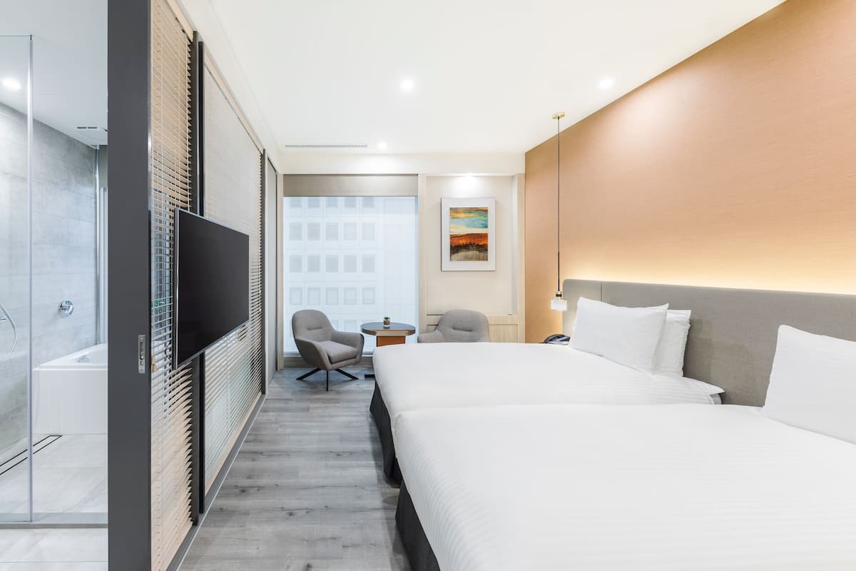 A hotel room with a large bed, a TV, a small table, two chairs, and a shower area.