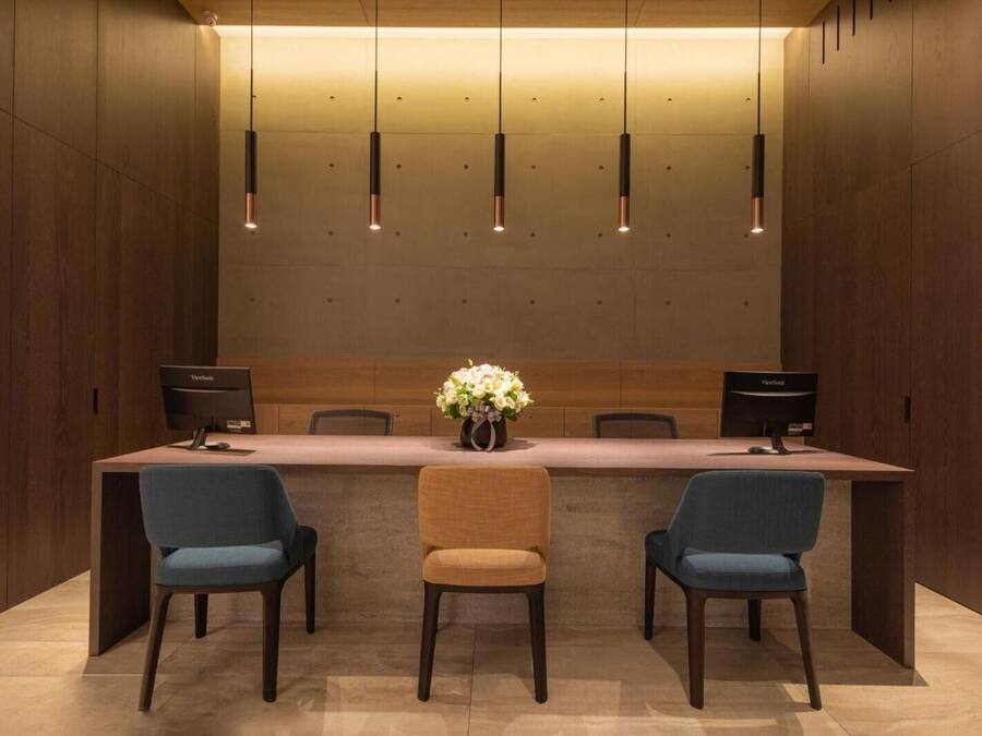 A conference room with a long table, three chairs, two monitors, and a vase of flowers.