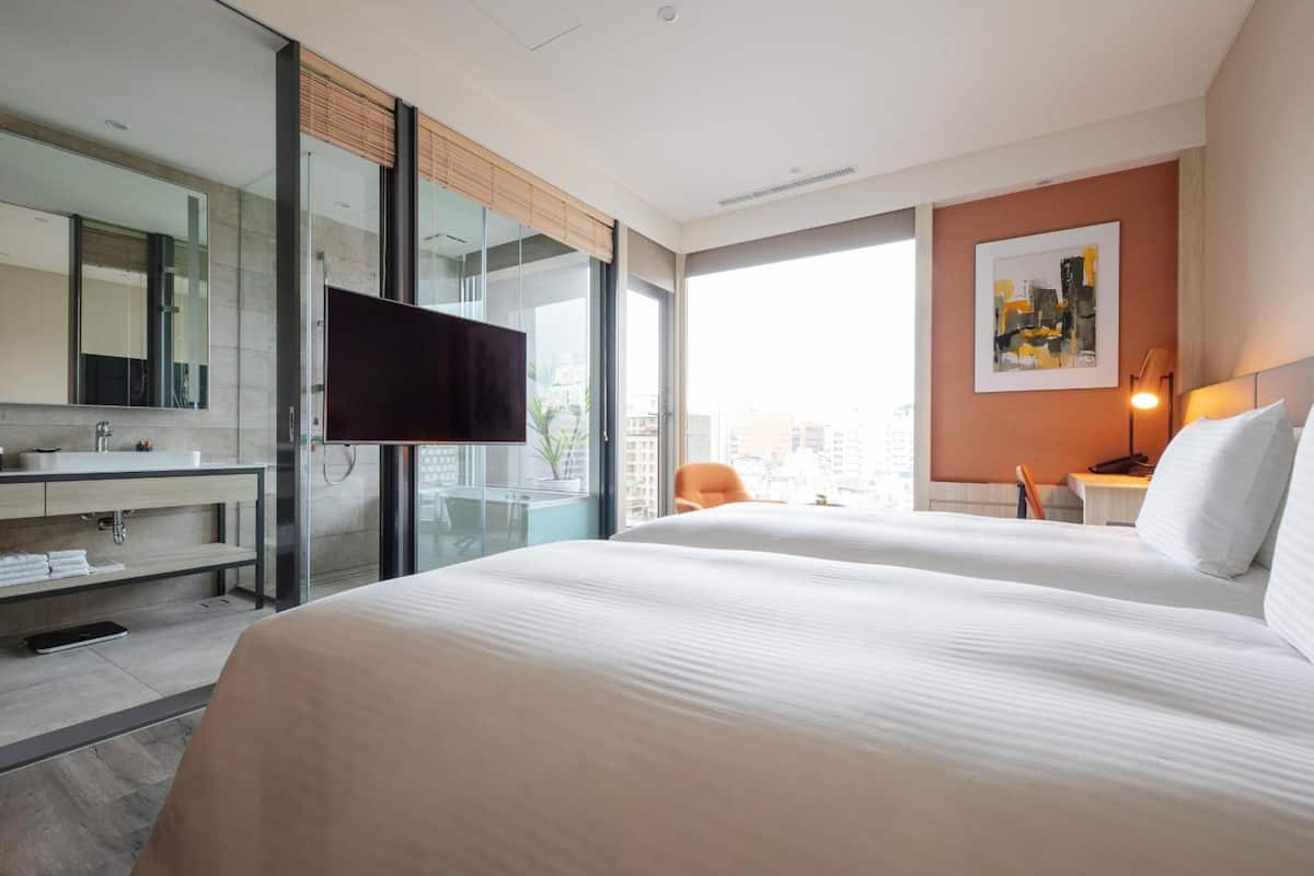 A hotel room with a large bed, a TV, a bathroom with a mirror, and a city view.