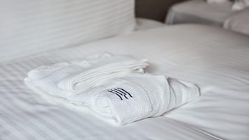 A neatly made bed with white linens and a folded towel on top.