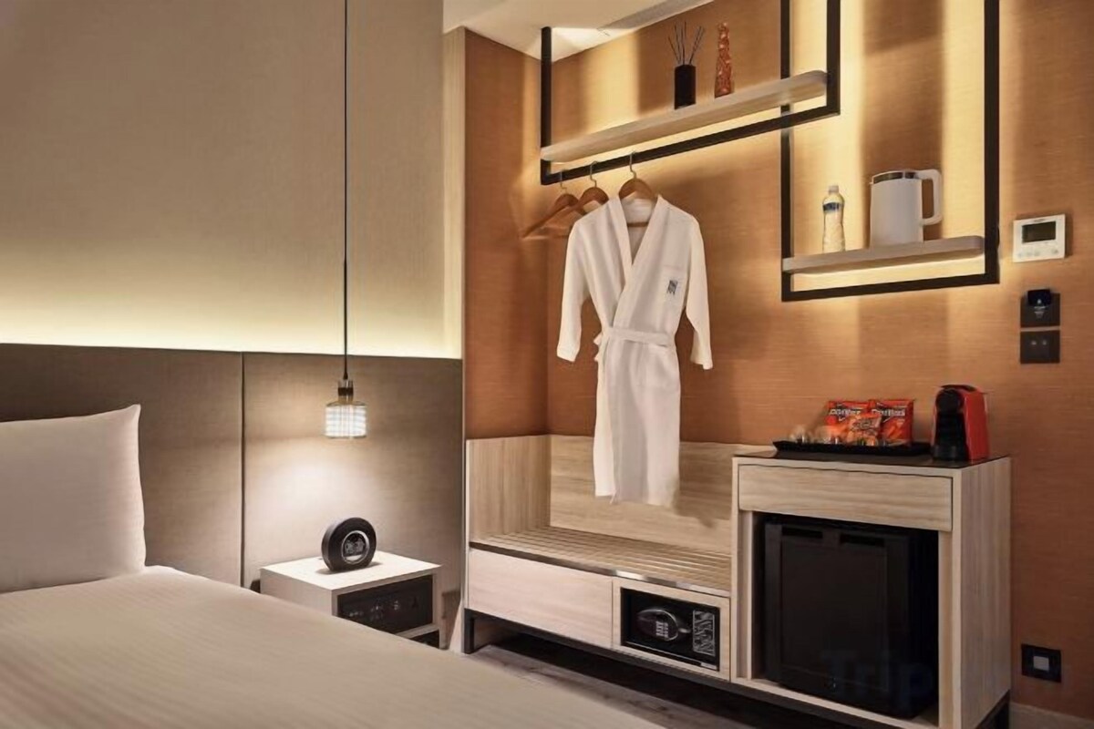 A hotel room with a bed, bedside table, nightstand, and a mirror with a robe hanging.