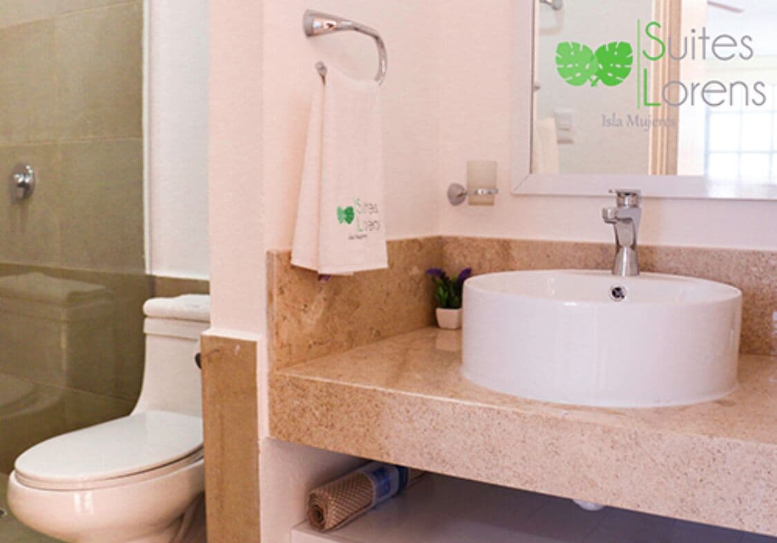 A bathroom with a toilet, sink, and mirror. A towel hangs on the wall.
